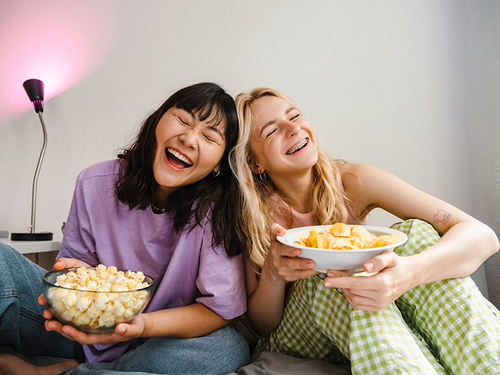 Two women laughing with bowls of snacks
