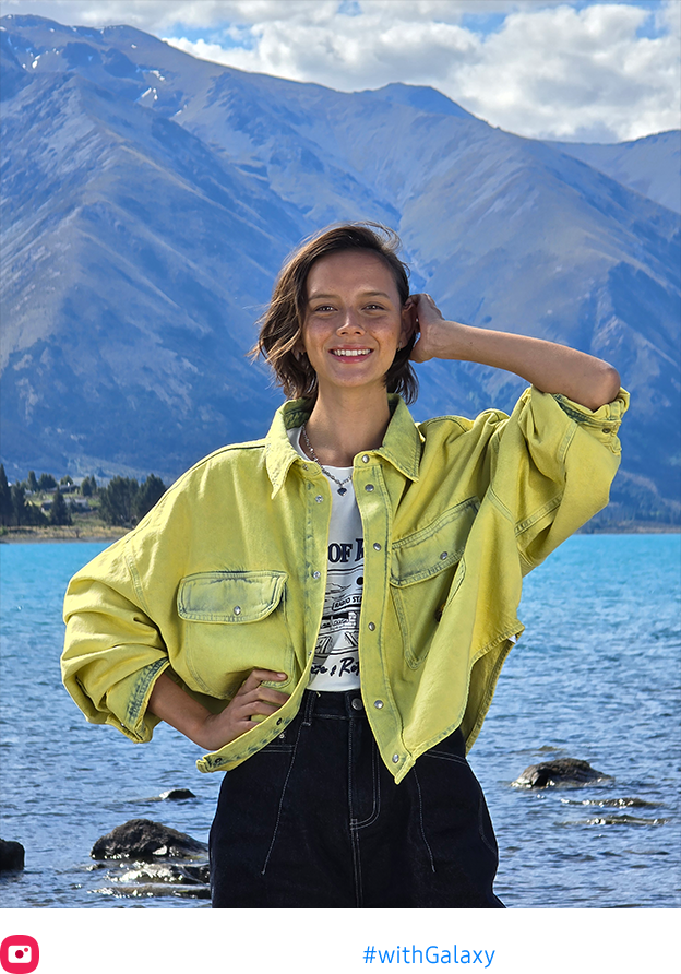 A photo taken at 6.5x zoom of a woman posing at a lake is vibrant and the mountainous scenery in the background is crisp.