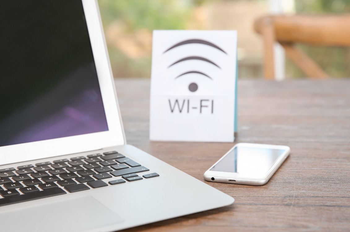 Computer and cell phone on table with a sign signifying Wi-Fi connectivity at this business