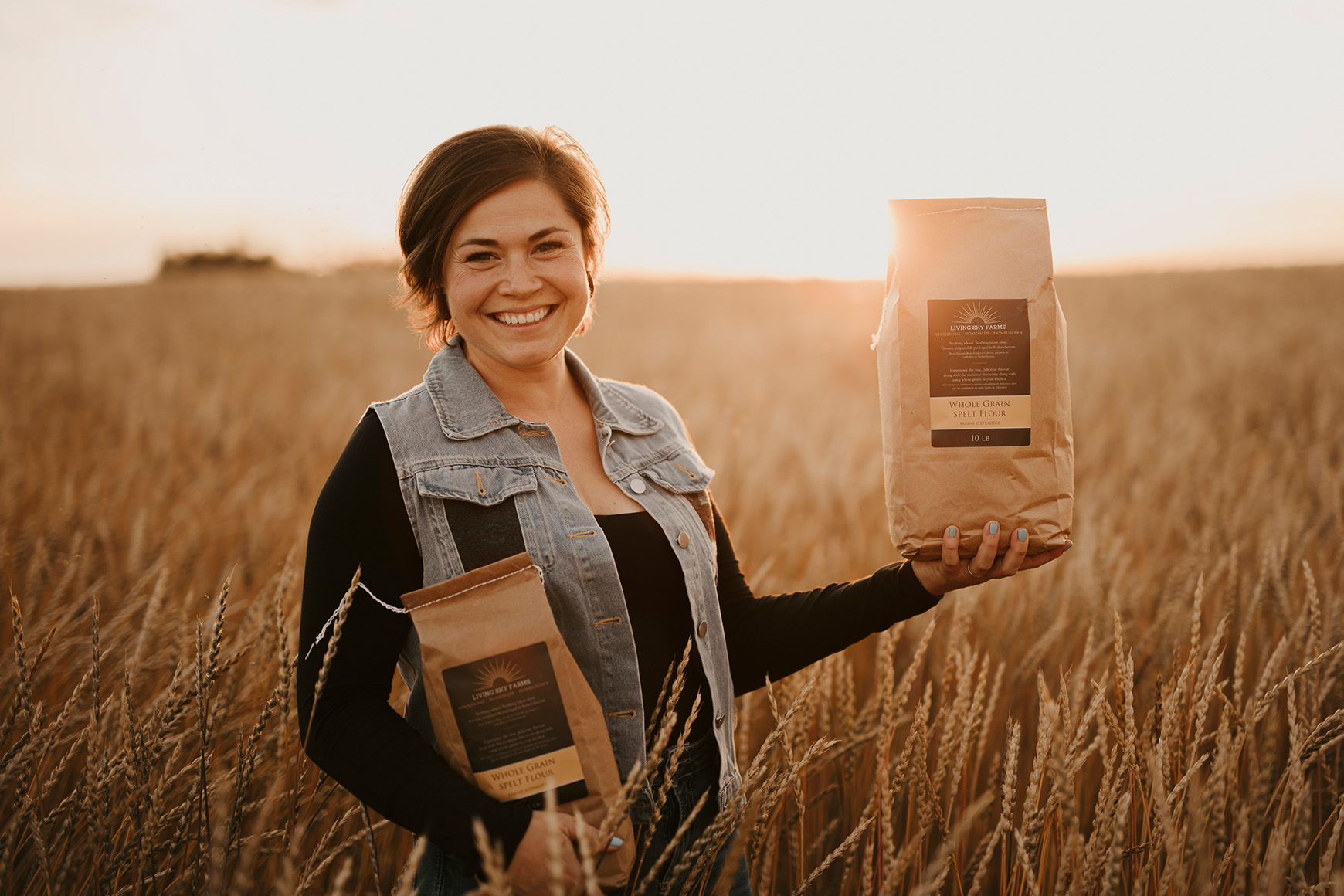 Living Sky Business Owner standing in a wheat field holding bags of their products