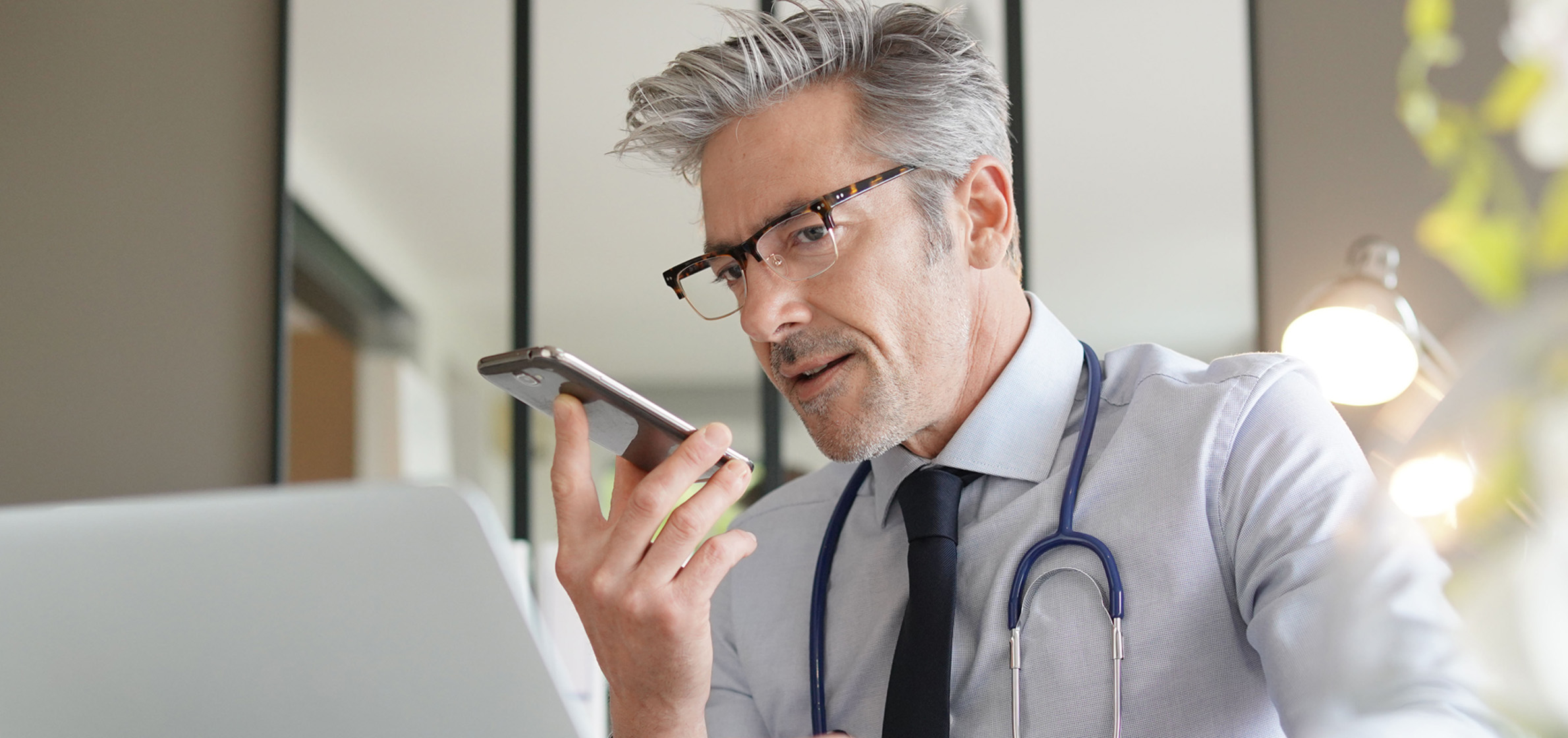 Doctor talking on cellphone handsfree sitting at laptop