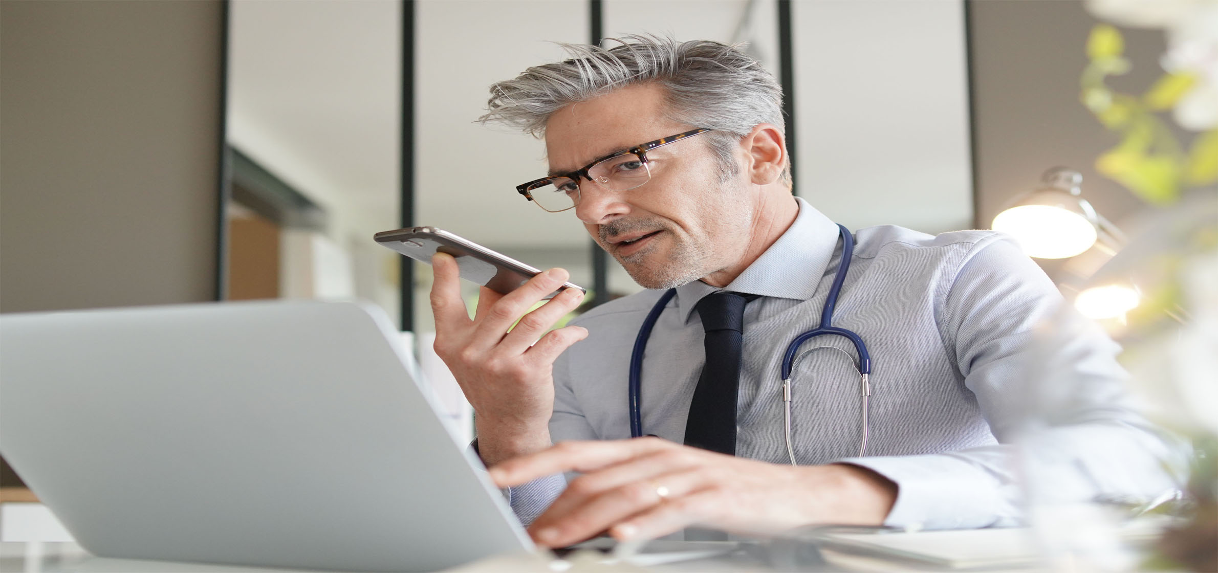 Doctor talking on cellphone handsfree sitting at laptop