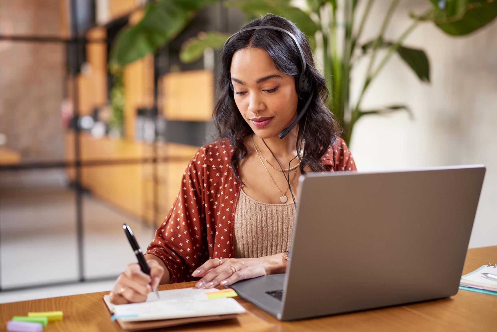 woman writing in notebook with laptop open in front of her